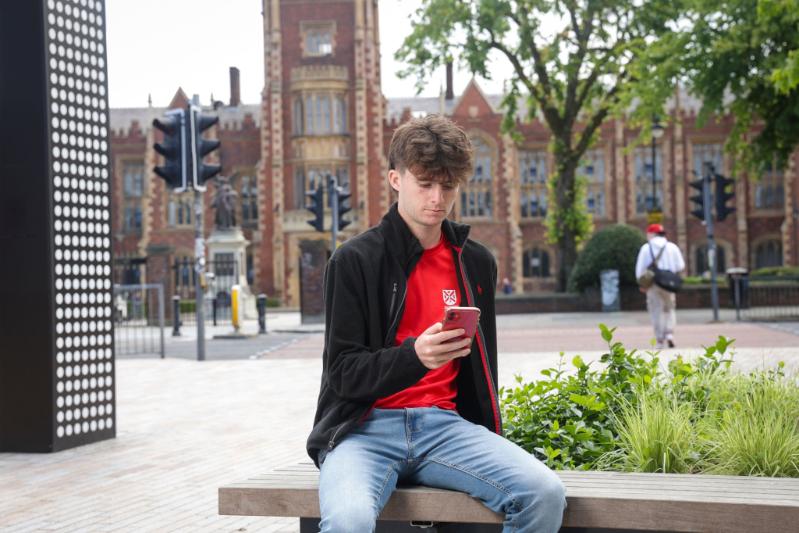 student looking at phone across from main Queen's building